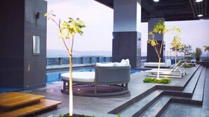A rooftop pool area with lounge chairs, a circular seating area, and small trees.