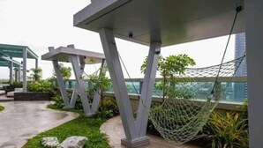 A modern outdoor area with a hammock, geometric seating, and a view of a cityscape.