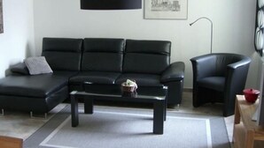 A modern living room with a black leather sofa, a black coffee table, and a black armchair. - Ferienwohnung Leuchtfeuer (Eckernförde)
