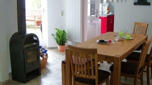 A dining area with a wood-burning stove, a table, chairs, and a potted plant. - Ferienwohnung Leuchtfeuer (Eckernförde)