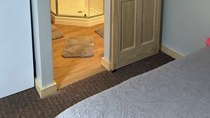 A room with a sliding door leading to a glass shower area, a bed with a patterned bedspread, and a wooden floor. - Small Space with a BIG View!!! (Redfield)