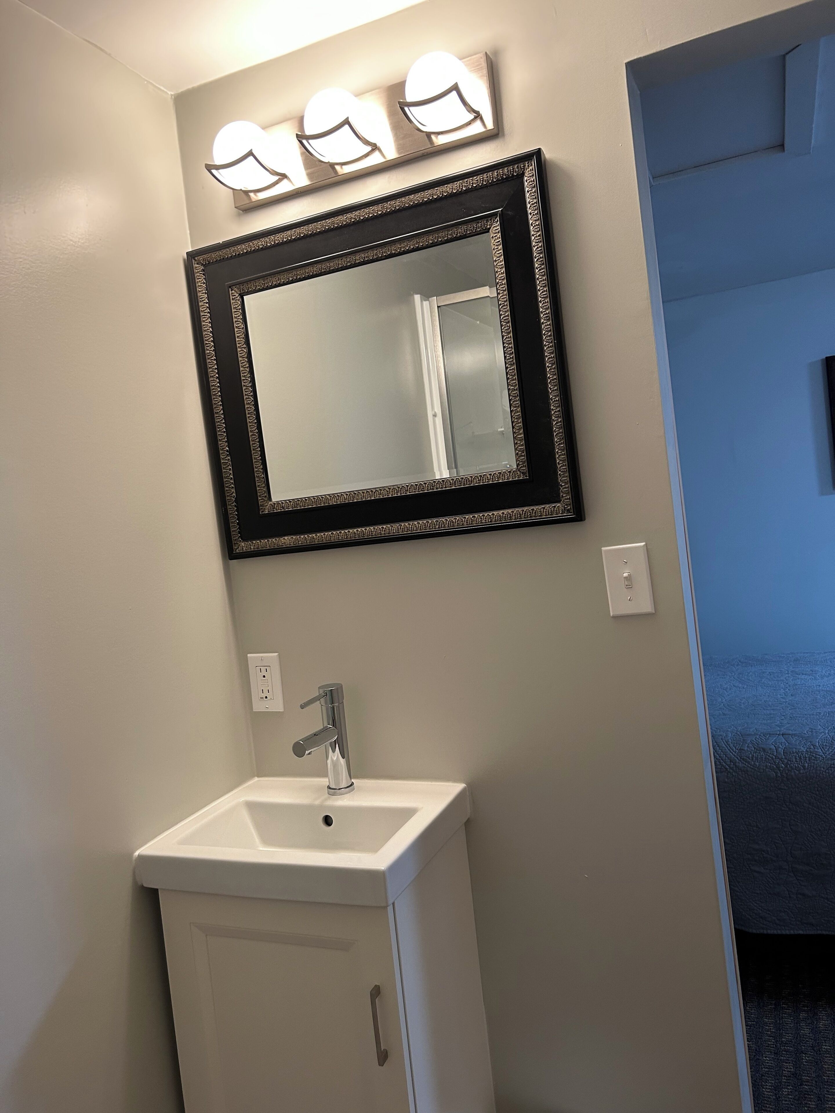 A bathroom with a white sink, a mirror with a decorative frame, and three wall-mounted lights.