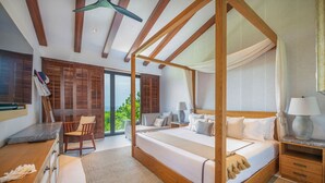 Un dormitorio espacioso con cama con dosel, un área de descanso con una silla y una mesa, y vistas a zonas verdes.