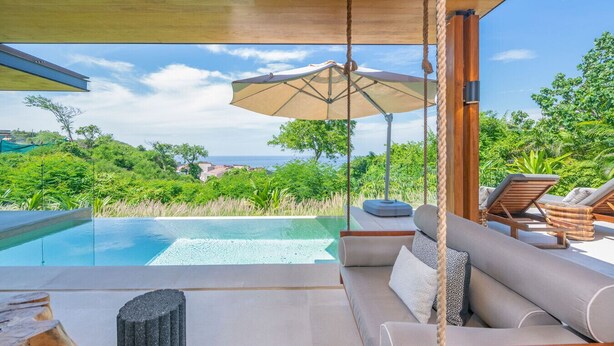 Un espacio exterior de lujo con piscina, con vistas a un paisaje exuberante y el océano.