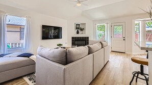 A modern living room with a grey sectional sofa, a flat-screen TV mounted on the wall, a ceiling fan, and a fireplace.