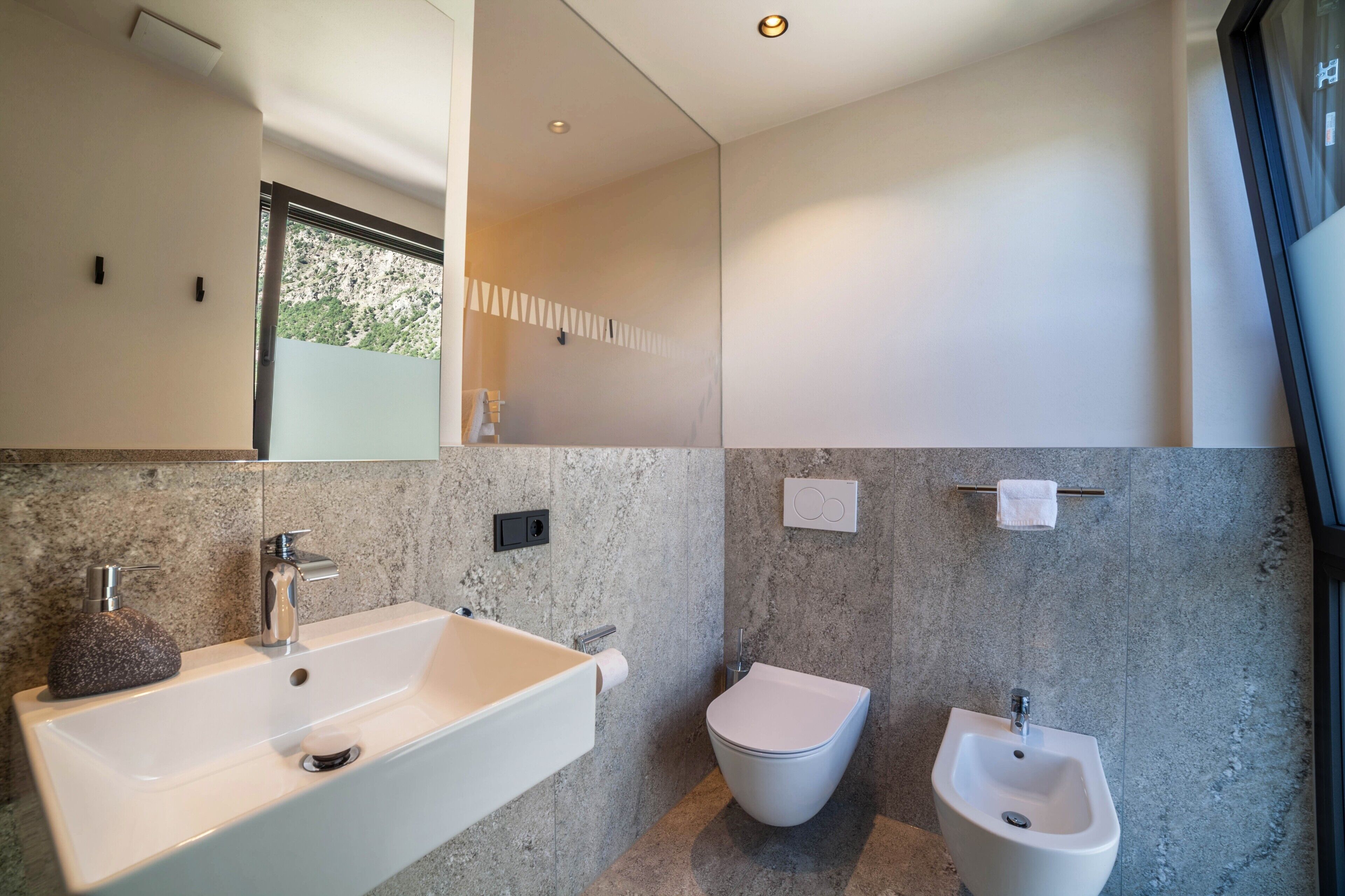 Een moderne badkamer met een groot wastafel, toilet, bidet en een spiegel boven de wastafel.