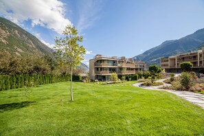 A modern building with multiple balconies, surrounded by a well-maintained lawn and a mountain backdrop.