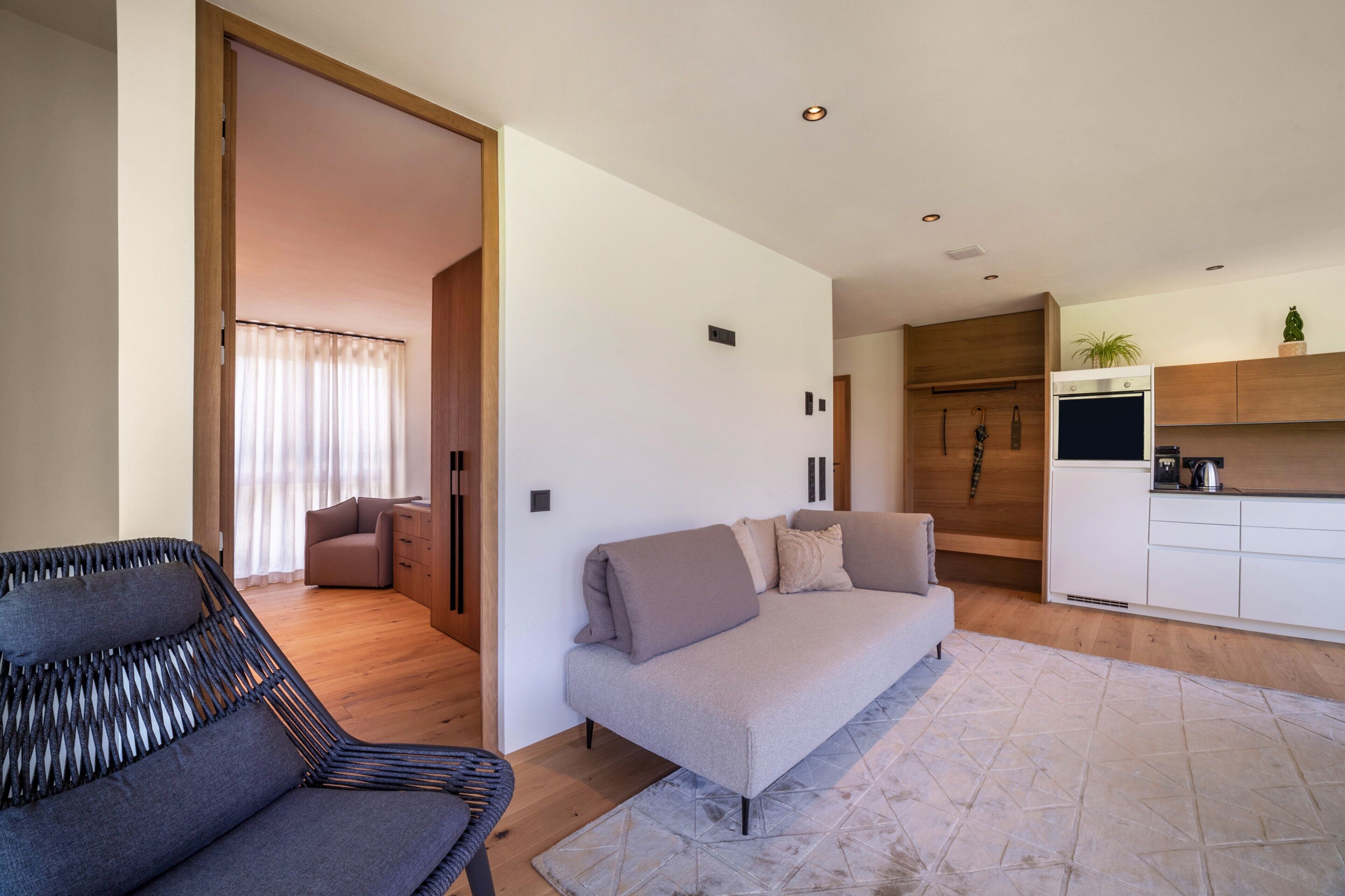 Een moderne woonkamer met een bank, een stoel, een keukenhoek en een houten vloer.