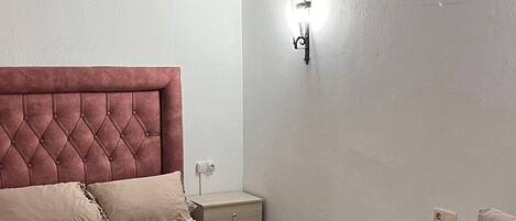 A bedroom with a bed, a nightstand, a chair, and an air conditioning unit.