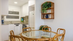 A dining area with a glass-top table surrounded by wicker chairs, a kitchen in the background, and a decorative plant shelf on the wall. - Holiday Apartment "Aubi" with Open Terrace and Indoor Terrace (Palamós)