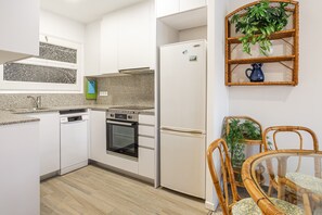 A modern kitchen with white cabinets, granite countertops, a built-in oven, a refrigerator, and a dining area with wicker chairs and a glass table.