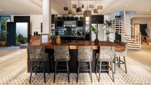 A modern kitchen with a central island, bar stools, and a staircase leading to an upper level.