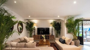 A modern living room with beige sofas, a wooden coffee table, and large potted plants.