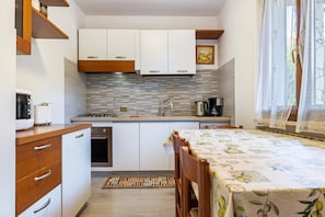 A compact kitchen with white cabinets, a tiled backsplash, and a dining area with a table set for two.