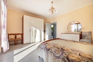 A bedroom with a bed, wardrobe, mirror, and a view of the outdoors.
