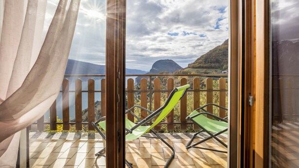 En balkon med udsigt over et bjergrigt landskab og et vandområde.