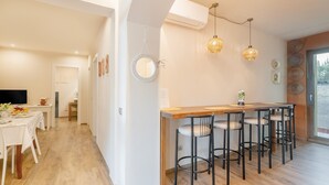 Una cocina moderna con barra de madera, taburetes de bar, luces colgantes y comedor con mesa dispuesta para cuatro.