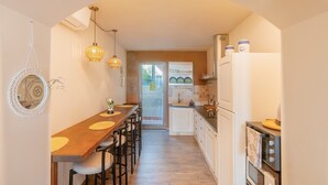 Cocina estrecha con una mesa de comedor de madera, luces colgantes y vista al área de comedor contigua.