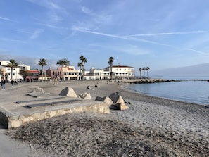 Ein Strand mit Gebäuden, Palmen und einer felsigen Küstenlinie.