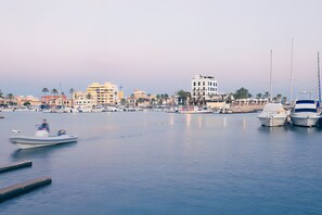 A marina with boats docked, a calm water body, and a cityscape with buildings in the background. - BluehousePortixol · Your home by the sea in Palma de Mallorca (Palma)