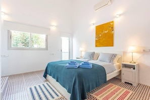 A bedroom with a bed, two bedside tables, a window, and a wall-mounted air conditioner. - BluehousePortixol · Your home by the sea in Palma de Mallorca (Palma)