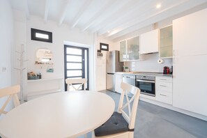 A modern kitchen with white cabinetry, a dining table with chairs, and a built-in oven. - BluehousePortixol · Your home by the sea in Palma de Mallorca (Palma)