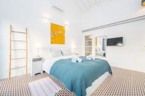 Ein Schlafzimmer mit Bett, Nachttischen, einer Lampe, einem Spiegel und einem an der Wand befestigten Fernseher.