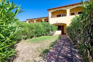 A building with a yellow facade, multiple balconies, and a pathway leading to the entrance. - Apartment "Baia delle mimose 50 meters from the sea" with shared pool, garden & A/C (Badesi)