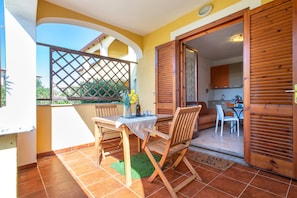 A balcony with a table and chairs, a wooden door, and a view of a kitchen.