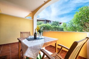 A patio with a table and chairs, a bottle, and a vase with flowers. - Apartment "Baia delle mimose 50 meters from the sea" with shared pool, garden & A/C (Badesi)