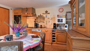 Een keuken met houten kastjes, een magnetron, een fornuis en een klok aan de muur.