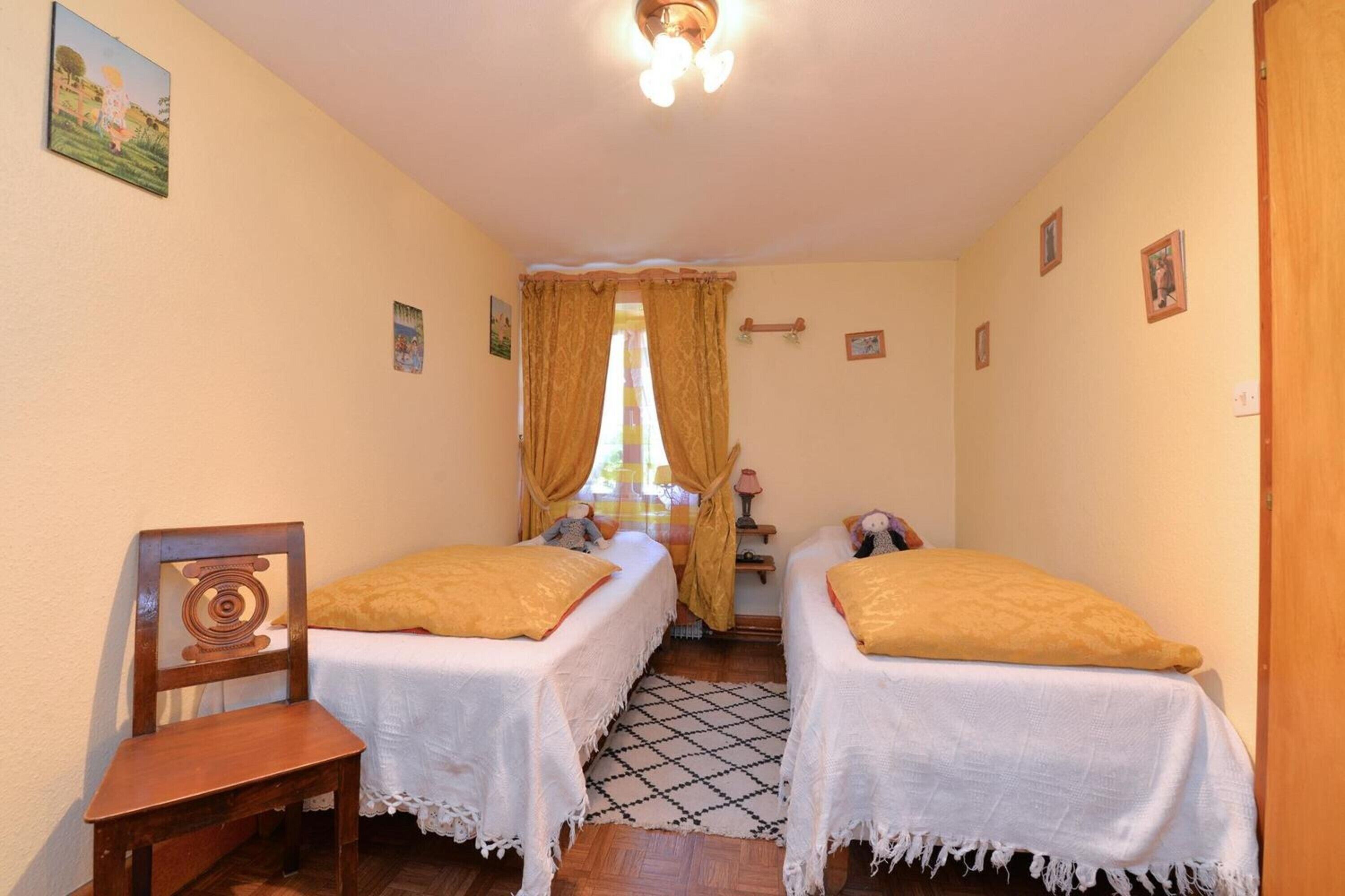 A room with two beds, a wooden chair, a small table, and a window with curtains.