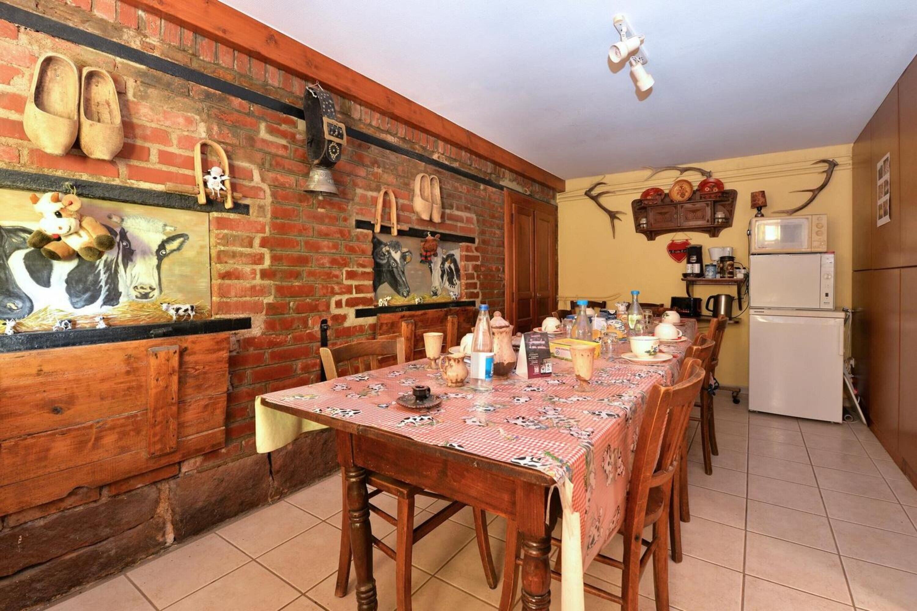 A dining area with a long wooden table, chairs, a red tablecloth, and various kitchen appliances.
