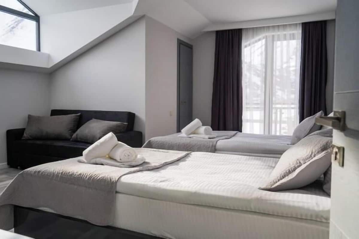 A hotel room with two beds, a sofa, and a large window with curtains.
