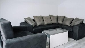 Un salon moderne avec un canapé d’angle noir, une table basse en verre et des fauteuils gris.