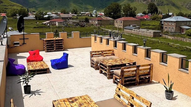 Un espace extérieur aménagé avec des meubles en bois et des coussins, offrant une vue sur un village et des montagnes.