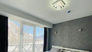 Une chambre moderne avec un grand lit, une vue sur l’extérieur grâce à une porte coulissante et un luminaire au plafond.