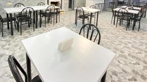Un espace repas moderne avec des tables blanches et des chaises noires, un mur en pierre et un éclairage encastré au plafond.