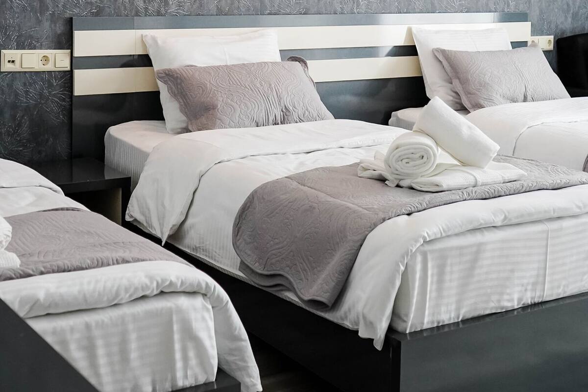 A hotel room with a modern design, featuring two beds with matching headboards, a grey textured wall, and a neatly arranged set of towels.
