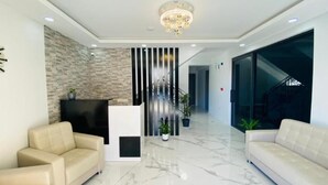 Un hall d’entrée moderne avec un comptoir d’accueil, deux canapés, un lustre et un escalier.