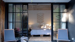 Quarto moderno com cama grande, luminária pendente e vista através de uma porta de vidro.