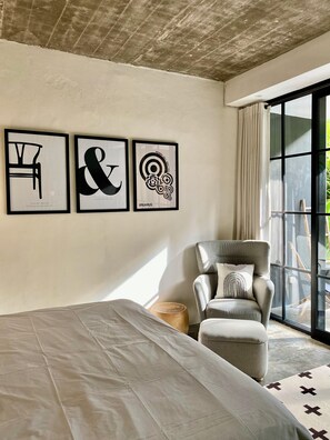A bedroom with a bed, a grey armchair, and three framed artworks on the wall. - The CIVYT (Ubud)
