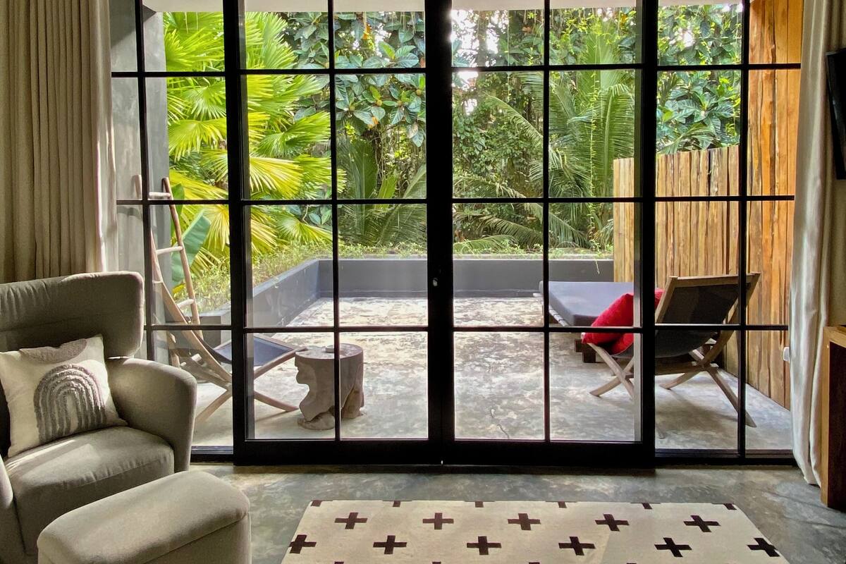 A room with a large sliding glass door leading to a patio with outdoor furniture and lush greenery.