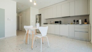 Een moderne keuken met witte kasten, een eettafel met stoelen en een inbouwmagnetron.