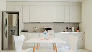 Een moderne keuken met witte kasten, een roestvrijstalen koelkast, een magnetron en een tafel met twee witte stoelen.