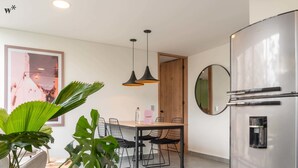 Eine moderne Küche mit einem Edelstahl-Kühlschrank, einem Esstisch mit Stühlen, Pendelleuchten und einer großen Pflanze.