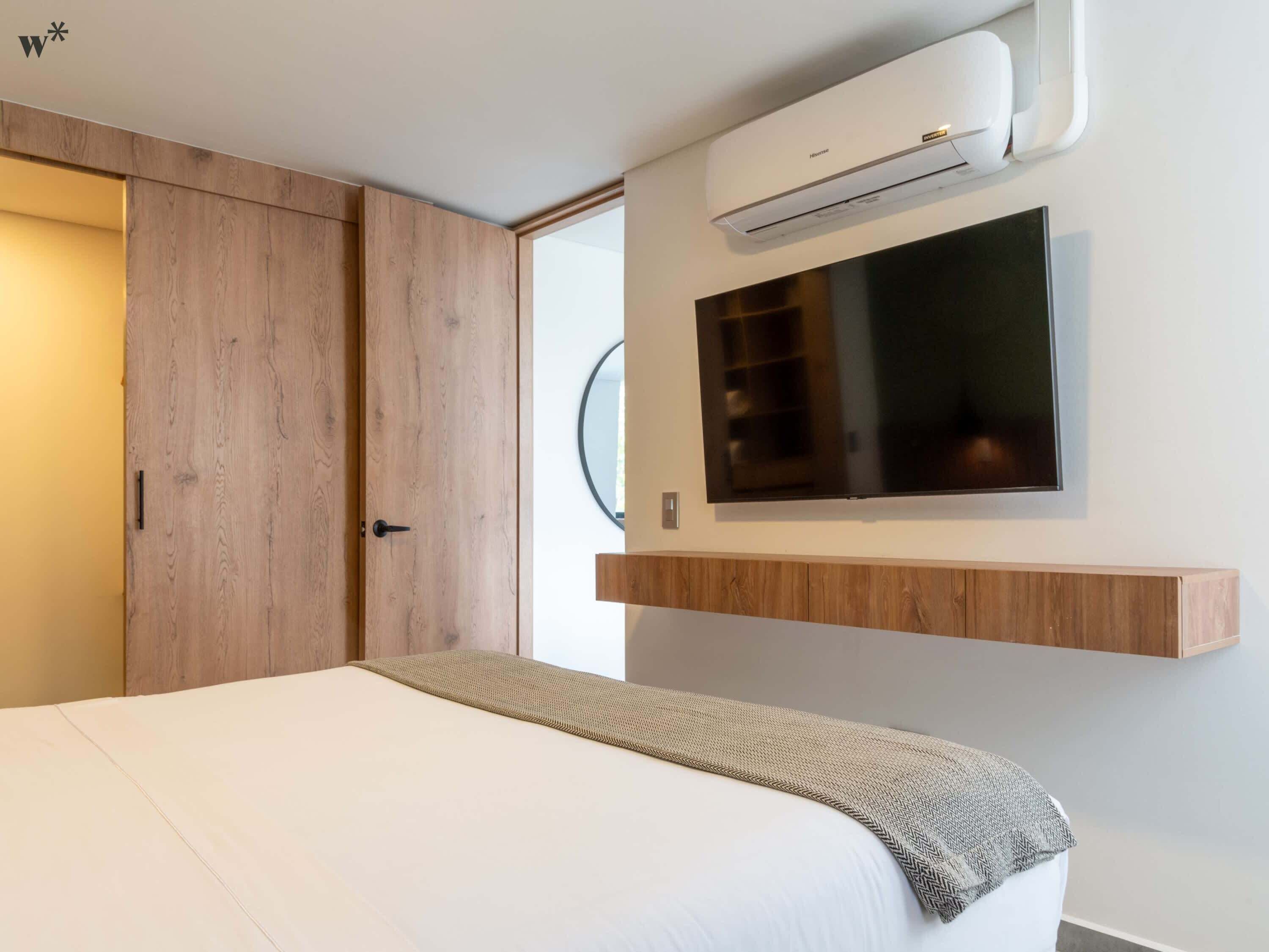 A modern bedroom with a bed, a mounted TV, and an air conditioning unit.