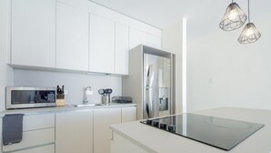 Een moderne keuken met witte kasten, een roestvrijstalen koelkast, een ingebouwde magnetron en een glazen kookplaat.
