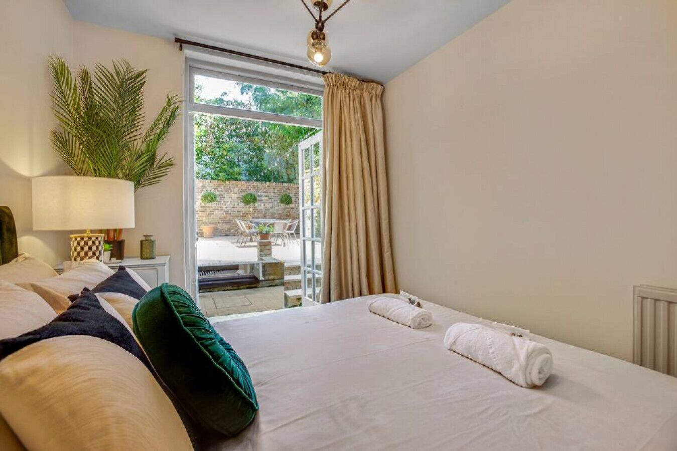Habitación de hotel con cama, mesita de noche, lámpara, planta en maceta y vistas del patio exterior.