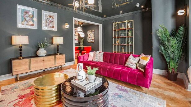 Un salon moderne avec un mur de couleur sombre, un canapé en velours rouge, un meuble en bois et une table basse décorative.